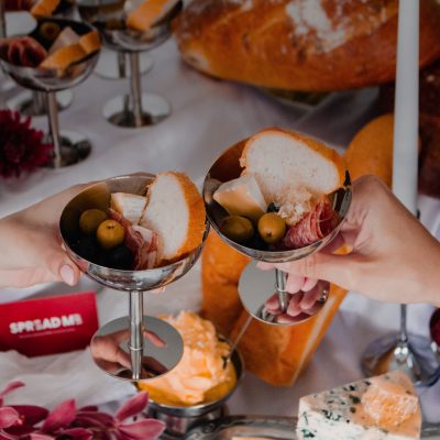 spread me grazing table two hands holding silver charcuterie cups